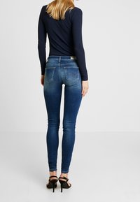 Kapeat siniset farkut haalistuneella viimeistelyllä, joissa on keskikorkea vyötärö, kaksi takataskua ja kontrastitikkaus. Pukeutuneena mustiin korkeakorkoisiin kenkiin.