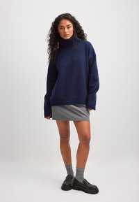 Tamsiai mėlynas per didelis megztinis su aukšta apykakle, su braižytomis apačia ir rankovėmis, derinamas su pilka mini sijonu, pilkomis kojinėmis ir juodais platforminiais batais.