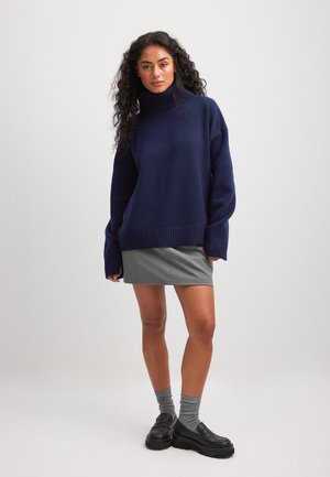 Tumedate sinine ülipikkade varrukatega turtleneck-sviiter, ribadega ääre ja mansettidega, kombineeritud halli mini-seeliku, hallide sokkide ja mustade platvormkingadega.