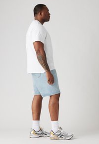 T-shirt en coton blanc, short en denim bleu clair, chaussures de sport argentées et dorées, vues de côté sur un fond neutre.