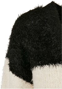 Tissu noir à texture duveteuse avec un matériau tricoté blanc cassé en dessous sur la zone de l'épaule d'un vêtement.