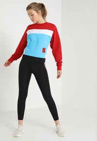 Felpa a blocchi di colore in rosso, bianco e azzurro, abbinata a leggings neri con strisce laterali rosa. Il materiale sembra morbido e flessibile.