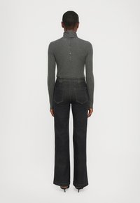 Col roulé gris à manches longues avec un dos boutonné, associé à un jean évasé bleu foncé avec poches arrière et taille haute.