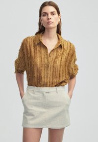 Brown textured button-up shirt with frayed detailing, paired with a light-colored textured mini skirt. Both garments feature a relaxed fit.