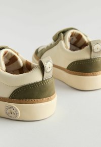 Kremowe i oliwkowozielone sneakersy z teksturowanym tyłem, wzorzystą wyściółką i zapiętką z motywem lwa. Wygodny design z gumową podeszwą.
