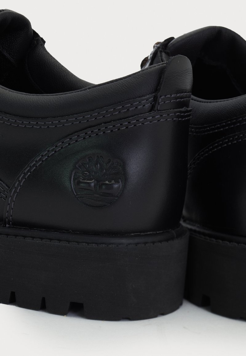 Black leather shoes featuring a smooth texture, rounded design, thick rubber sole, and embossed tree logo on the heel.