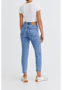 Jean skinny en denim bleu clair avec texture délavée, taille haute et poches arrière. Associé à des baskets blanches et un top court.