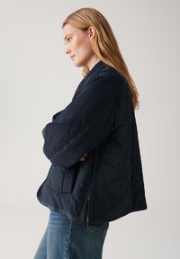Marineblauwe gewatteerde bomberjack met een relaxte pasvorm, voorzien van een rits en zijzakken. Zachte stof en een gladde textuur met een matte afwerking.