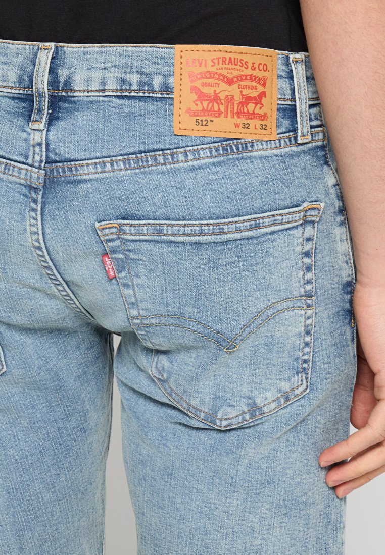 Jeans de mezclilla azul claro con costuras visibles, una etiqueta roja en el bolsillo trasero y un parche de cuero marrón etiquetado "Levi Strauss & Co."