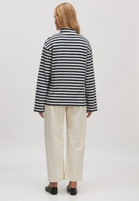 Gestreiftes Langarmshirt in Marineblau und Weiß, mit entspanntem Schnitt und rundem Ausschnitt, kombiniert mit cremefarbenen weiten Hosen und schwarzen Schuhen.