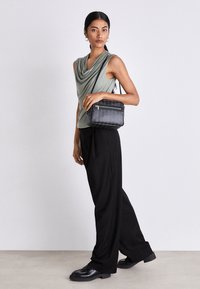 Borsa a tracolla nera con texture, dotata di tasca con zip, abbinata a una maglietta drappeggiata verde oliva e pantaloni neri con vestibilità ampia.
