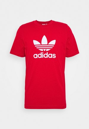 T-shirt rouge en coton avec un col rond, arborant un grand logo Adidas blanc et un graphisme à trois feuilles centré sur la poitrine.