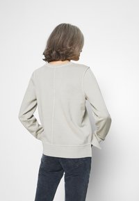 Sudadera de manga larga en gris claro con puños y dobladillo acanalados, que presenta un sencillo detalle de costura en la parte posterior. Fabricada en una suave tela texturizada.