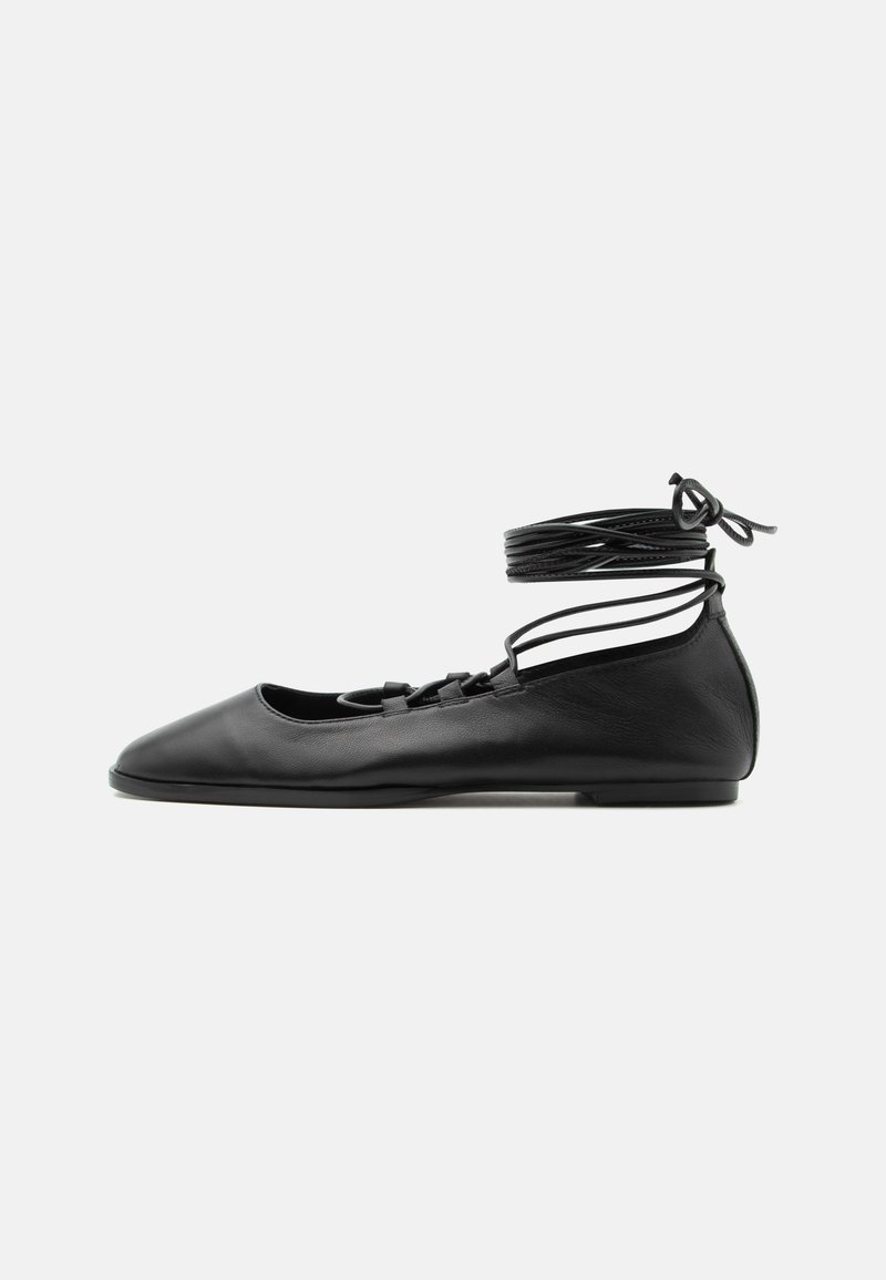 Chaussure de ballet plate en cuir noir avec un bout pointu, plusieurs fines brides sur le dessus et des lacets enroulés autour de la cheville.