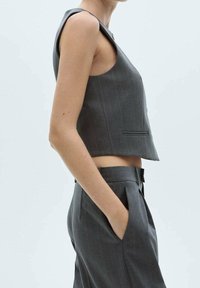 Grijze, mouwloze cropped jas met een rechte snit en een subtiel streepmotief. Gecombineerd met bijpassende high-waisted broek.