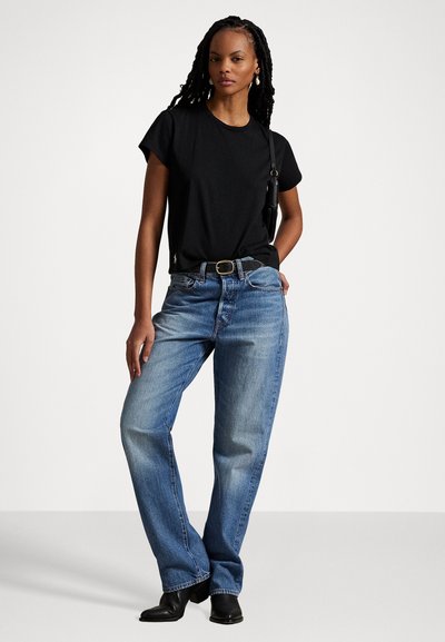 Black t-shirt, blue denim jeans, relaxed fit with slight distressing. Black belt with metallic buckle, ankle-length, worn with black boots.