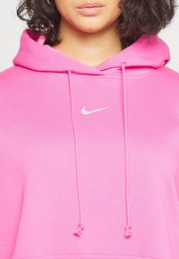 Pink hoodie made of soft fabric, featuring a front kangaroo pocket, drawstrings, and a small white Nike logo on the chest.