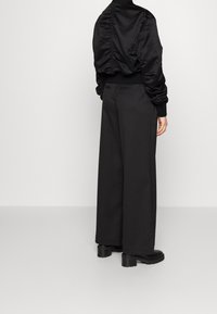 Zwarte satijnen bomberjack met gathered achterkant, gecombineerd met hoge taille wijdvallende zwarte broek en chunky zwarte laarzen.