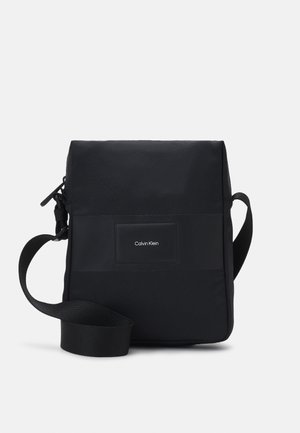 Borsa a tracolla nera realizzata in tessuto testurizzato, con forma rettangolare, tracolla regolabile e un'etichetta con logo sul davanti.