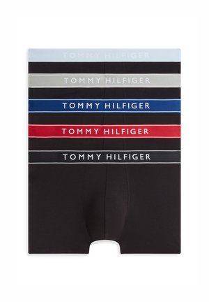 Mladý muž stojí bosý s prekríženými rukami, oblečený v čiernych boxerkách Tommy Hilfiger na jednoduchom bielom pozadí.
