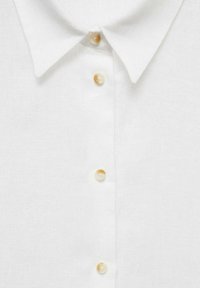 White linen shirt with a classic collar, featuring five round, light-colored buttons along the front placket. Smooth texture, simple design.