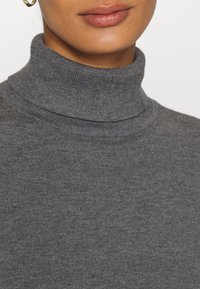 Pull à col roulé gris présentant une texture en tricot doux, une coupe ajustée et un col côtelé. Aucun motif visible ni détail de quincaillerie.