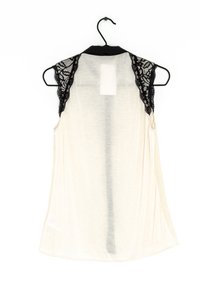 Cream tank top with black lace accents on shoulders, made of soft fabric, featuring a rounded hem and loose fit, displayed on a hanger.