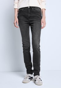 Czarne dżinsy o slim fit, z przednimi kieszeniami, z zapięciem na zamek i delikatnym wypłowieniem. Połączone z neutralnymi sneakerami.