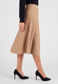Gonna midi plissettata beige realizzata in morbido tessuto, con una cintura larga. Abbinata a tacchi alti in suede neri.