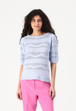 Un pull en tricot bleu clair à manches courtes, comportant un motif zigzag texturé et une bordure côtelée. Associé à des pantalons roses.