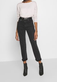 Jean noir taille haute avec une coupe slim et ourlet brut, assorti à un pull fin à manches longues rose clair et des bottines noires.