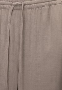 Světlé hnědé volné kalhoty vyrobené z prodyšné látky s texturovaným povrchem, s elastickým pasem a stahovací šňůrkou.