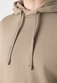 Sweat à capuche beige à texture douce, doté de cordons tressés et du logo "HUGO" en ton contrastant sur la poitrine.