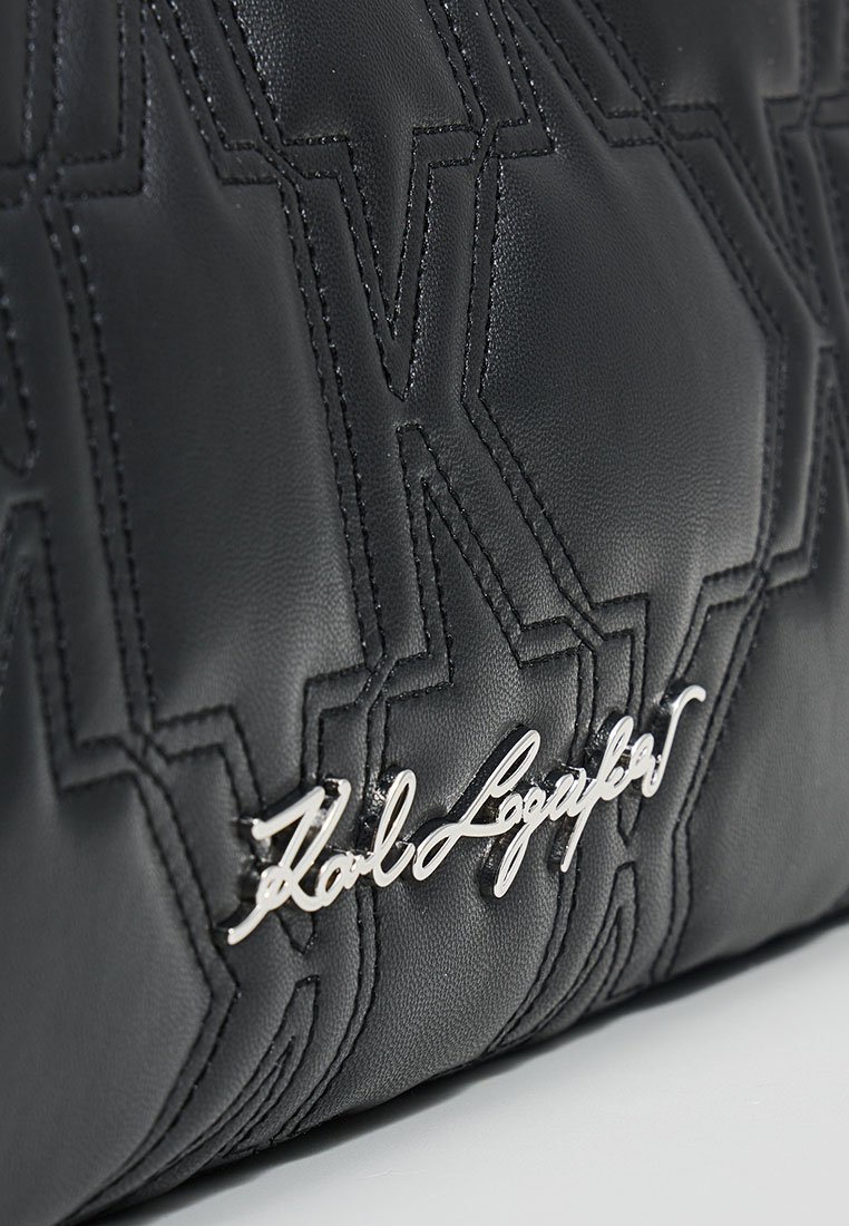 Sac à main en cuir noir avec un motif matelassé et un détail de logo en ton argenté. Texture lisse avec un design structuré.
