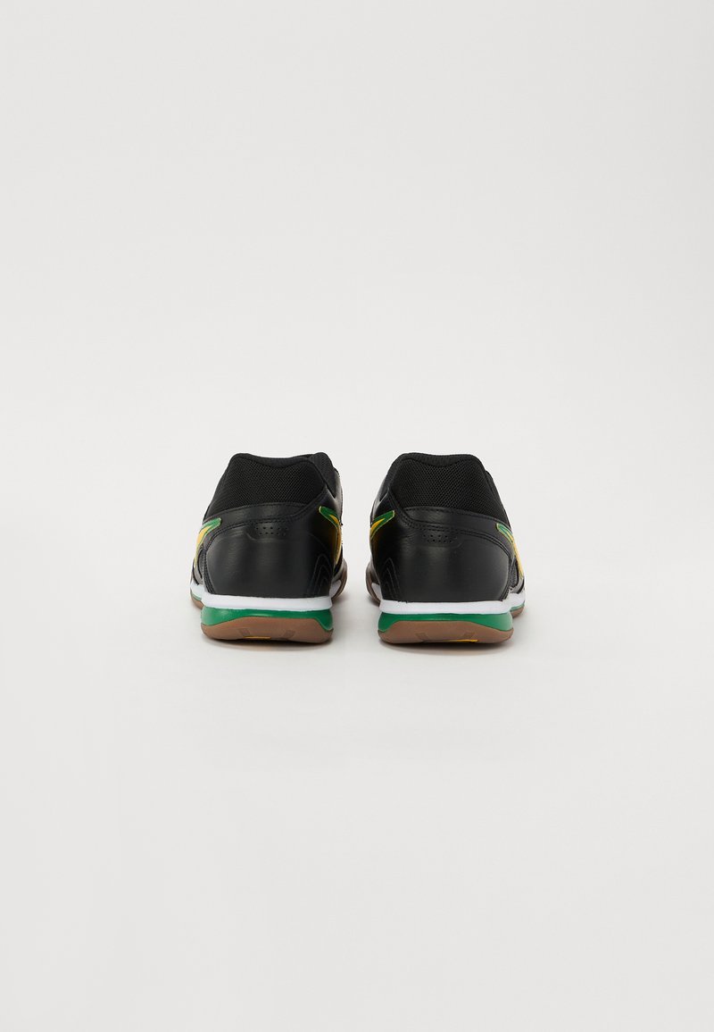 Zapatillas deportivas negras con una parte superior de malla, acentuadas con detalles en amarillo y verde, que presentan una suela texturizada y un soporte acolchado para el talón.