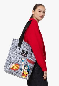 Tote-väska med grafik i serietidningsstil i svartvitt, med färgglad Wonder Woman-bild och text; tillverkad av hållbart material, med svarta remmar.