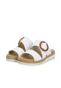White slide sandals featuring two wide straps and a large brown circular buckle. Soft, cushioned footbed with a textured, jute-like sole.