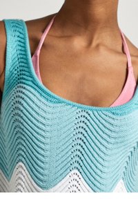 Kvinna i blå och vit stickad linne över en rosa bikinitopp, vilket visar nyckelbenet och halsområdet.