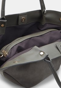 Borsa grigia in pelle liscia con una struttura morbida in suede. Presenta un compartimento con zip e dettagli decorativi in oro.