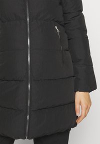 Chaqueta de plumón negra con diseño de acolchado horizontal, bolsillo lateral con cremallera, cremallera plateada y textura suave y ligera.