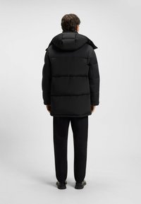 Sort puffer-jakke med en aftagelig hætte, med en quilted design og en afslappet pasform. Båret med sorte bukser og sko.