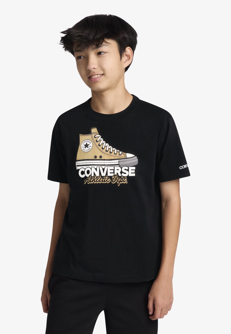 Μαύρο βαμβακερό T-shirt με γραφικό μπεζ υπερυψωμένου αθλητικού παπουτσιού Converse και κείμενο «CONVERSE Athletic Dept.» σε λευκό και χρυσό.