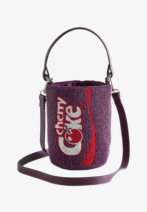 Sac seau violet en perles avec poignée supérieure et longue bandoulière, présentant un texte et un design "cherry coke" en rouge et blanc sur le devant.