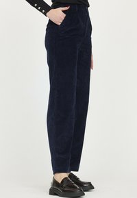 Pantalons en velours côtelé bleu marine avec une coupe droite, poches avant et texture subtile. Associés à des mocassins sombres pour un look complet.