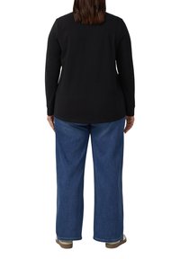 Zwarte longsleeve gecombineerd met loszittende blauwe jeans. De jeans hebben een standaard tailleband en zijn aan de onderkant iets gefranjerd.