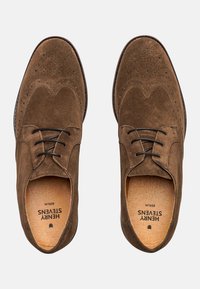 Chaussures en daim marron à lacets avec un design brogue, présentant un embout rond et de subtiles perforations sur la tige. Semelle intérieure en cuir visible.