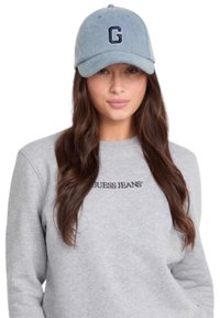 Cappellino da baseball in denim azzurro con un logo "G" blu scuro. Abbinato a una felpa grigia con la scritta "GUESS JEANS" in testo nero.