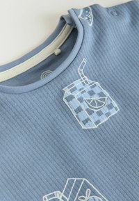Tela azul acanalada con cartones de bebidas estampados a cuadros que presentan rodajas de limón y pajitas sobre un material suave para ropa.
