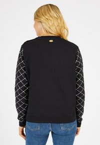 Sweat-shirt noir avec des manches matelassées ornées de pois blancs. Il présente un col rond et un détail de bouton à l'épaule.