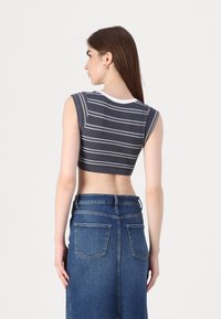 Top scurt cu dungi gri, cu borduri albe, asociat cu o fustă din denim albastru cu talie înaltă. Materialul pare texturat, având un design ajustat.